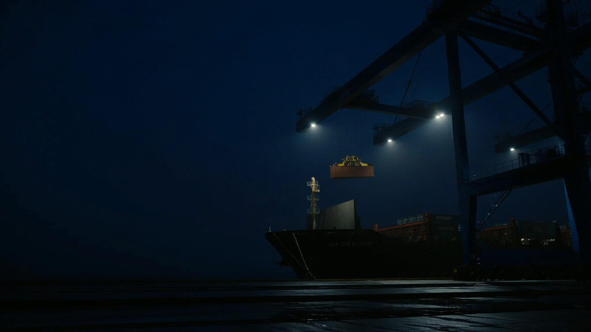 Grúa pórtico levantando un contenedor en un puerto de noche